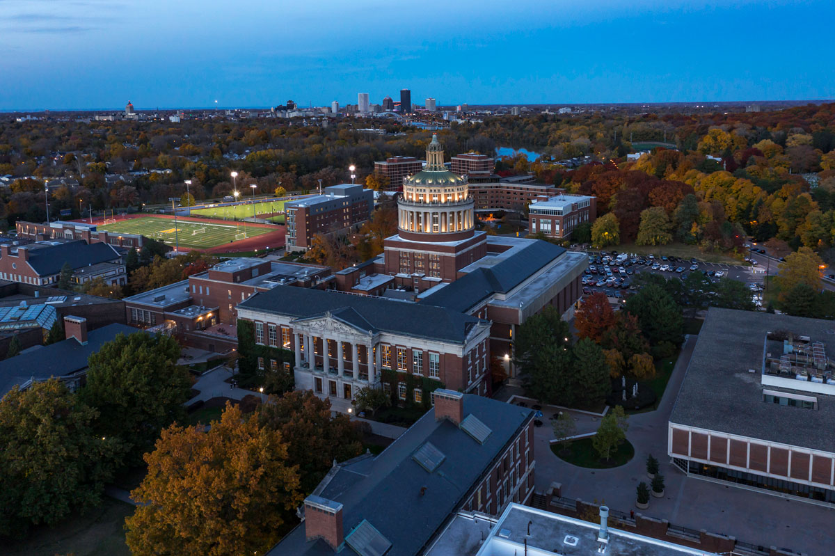 Aerial view of the University of Rochester campus at dusk, highlighting the library building amidst the serene twilight.