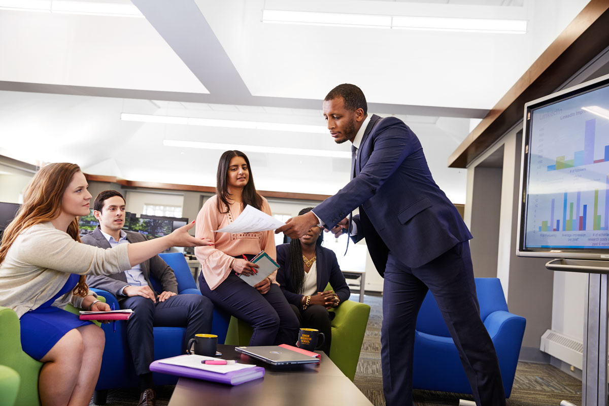 A diverse group of individuals engaged in discussion around a table in a University of Rochester meeting room.